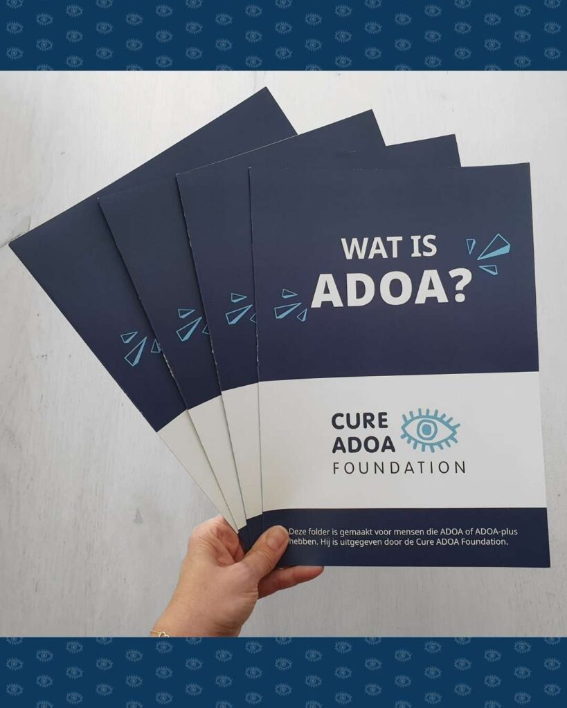 Een hand met een stapel folders van de Cure ADOA Foundation.