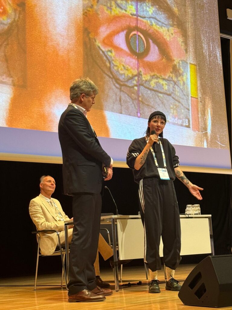 Kirsten Smit wordt geïnterviewd door Jan-Willem Pott. Achter hen een projectie van de scan van een oog.