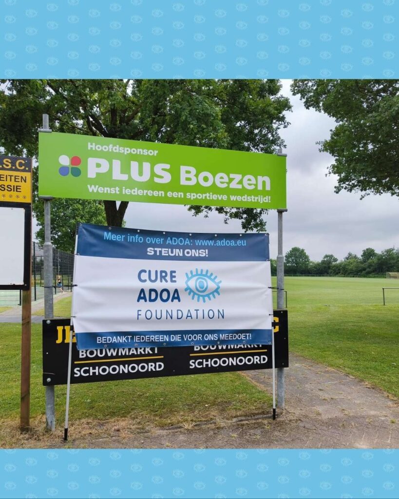 Een spandoek van de Cure ADOA Foundation staat langs de weg.