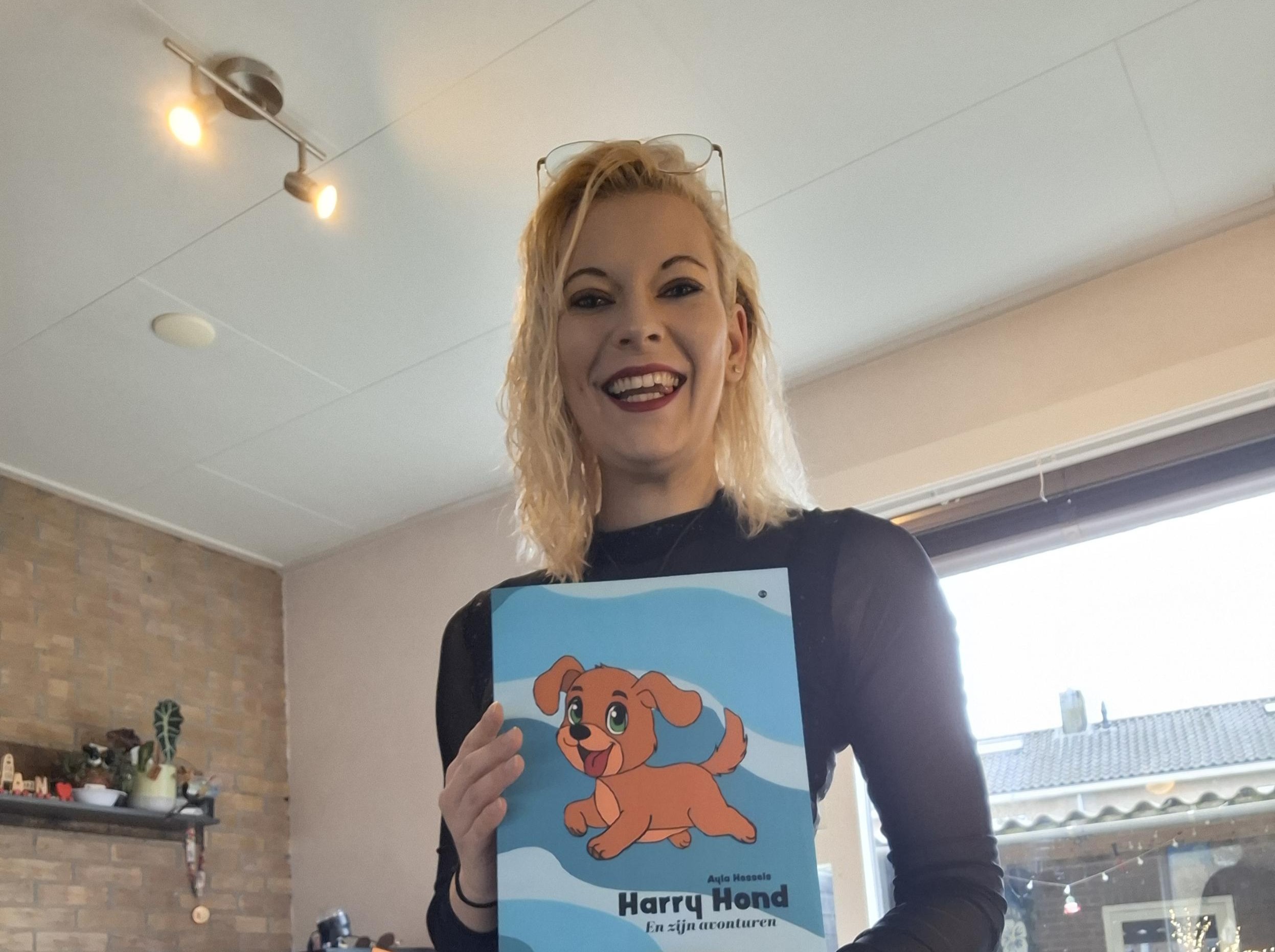 Ayla, een witte vrouw met halflang geblondeerd haar. houdt haar boek Harry Hond vast. Ze kijkt blij.