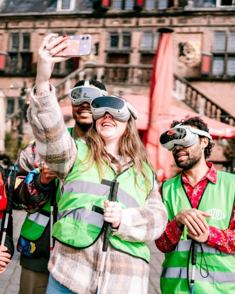 Bezoekers muZIEum met VR-brillen, taststokken en opvallende hesjes maken lachend een selfie.