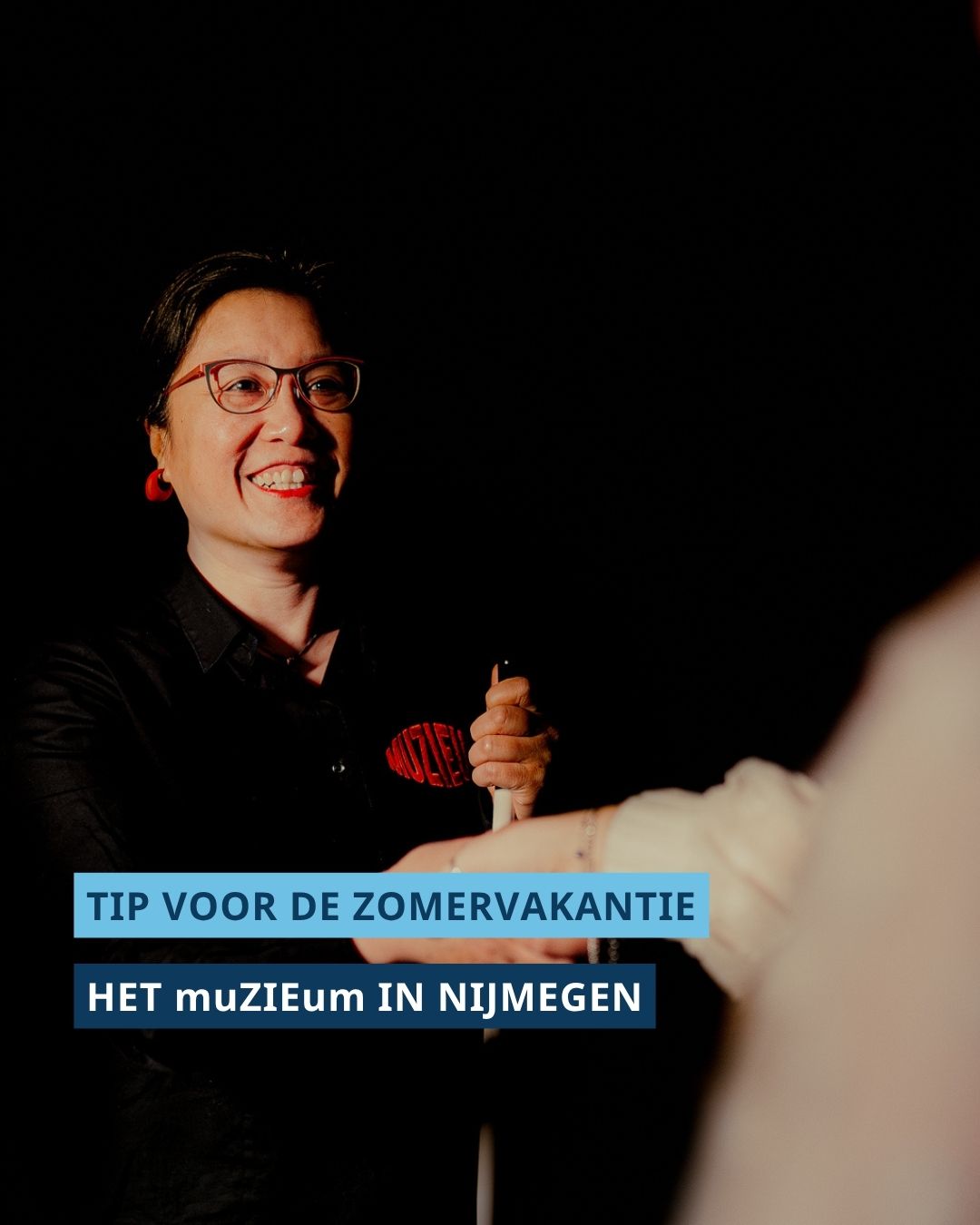 Gids met taststok stelt zich in een donkere ruimte voor aan een bezoeker.