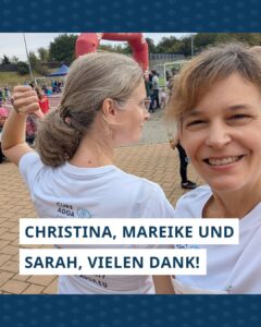 Foto van Sarah en Mareike. Sarah staat met haar rug naar de camera en wijst naar de tekst op haar shirt, waar onder andere het logo van de Cure ADOA Foundation te zien is. Mareike lacht in de camera. Onder de foto staat de tekst ‘Christina, Mareike und Sarah, vielen Dank!’