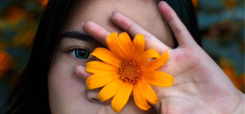 Vrouw houdt oranje bloem voor haar linkeroog.
