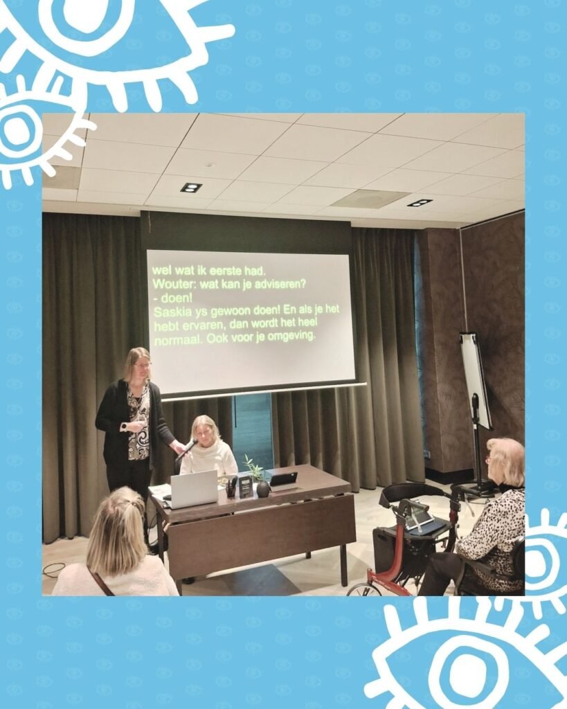 Saskia te Hoeve zit achter een bureau voor de groep en spreekt over haar ervaringen. Met hulp van schrijftolk Afke Hop verschijnt haar verhaal achter haar op een beamer.