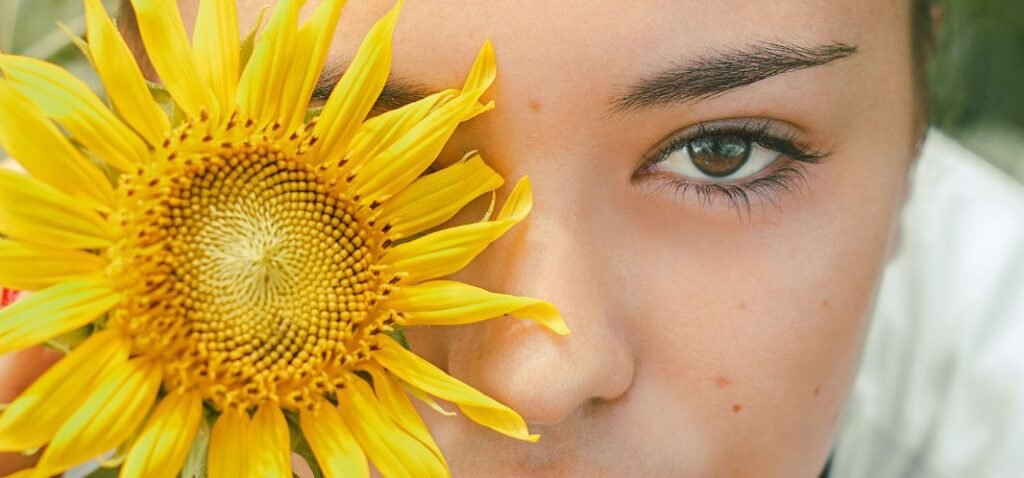 Portret van vrouw die gele zonnebloem voor rechteroog houdt.